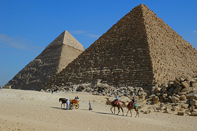 エジプトのピラミッドの前でラクダに乗る人々の写真